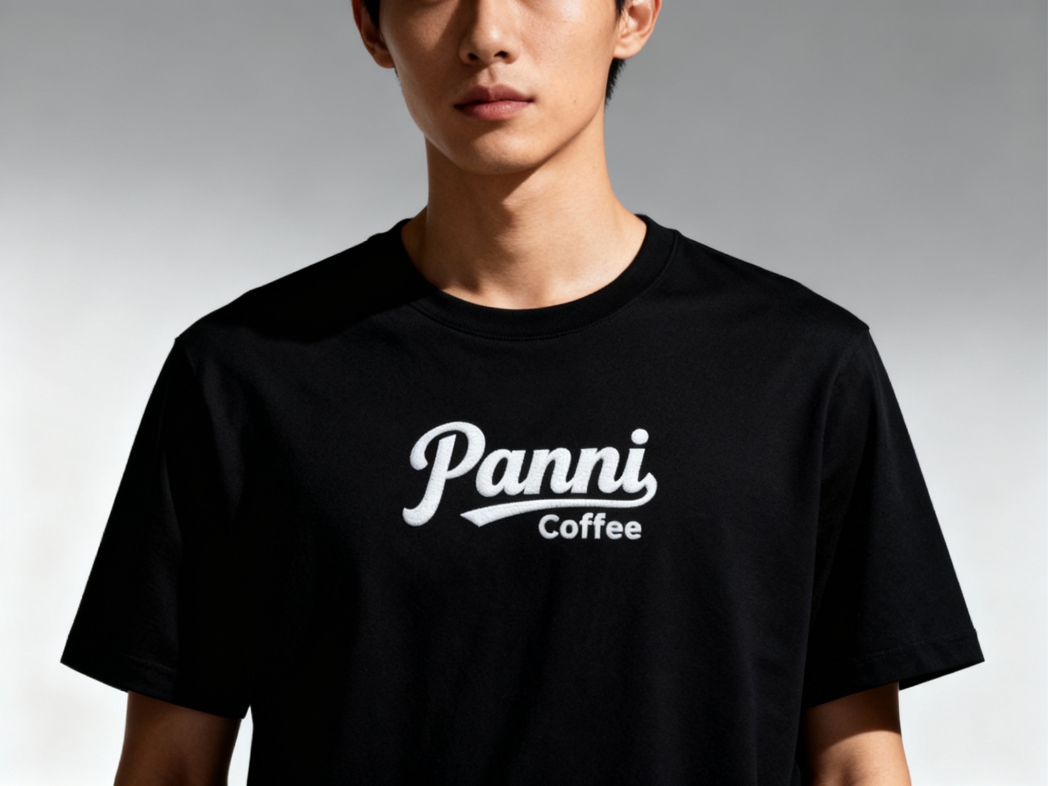 提取参考图的LOGO单独呈现，改为白色，25岁亚洲男性模特，身着纯黑哑光T恤，白色LOGO以胶浆印花工艺呈现在胸口中央，边缘平整细腻，侧逆光拍摄，光线勾勒模特肩部线条，T恤质感柔软垂顺，背景为极简灰色渐变，4A广告大片质感，视觉焦点集中于LOGO