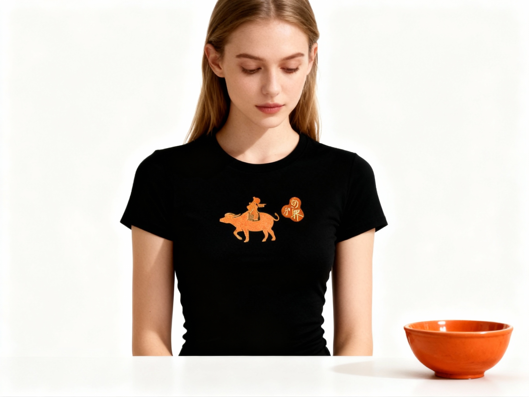 提取参考图的LOGO单独呈现，改为橙色，25岁欧洲女性模特，穿黑色修身T恤，橙色LOGO采用烫金工艺印制，金属光泽细腻不浮夸，正面柔光拍摄，光线均匀照亮T恤表面，凸显LOGO与面料的质感对比，模特自然垂眸，背景为纯净白色，画面简洁高级，旁边放置一个橙色陶瓷碗，与LOGO颜色呼应，增添东方韵味