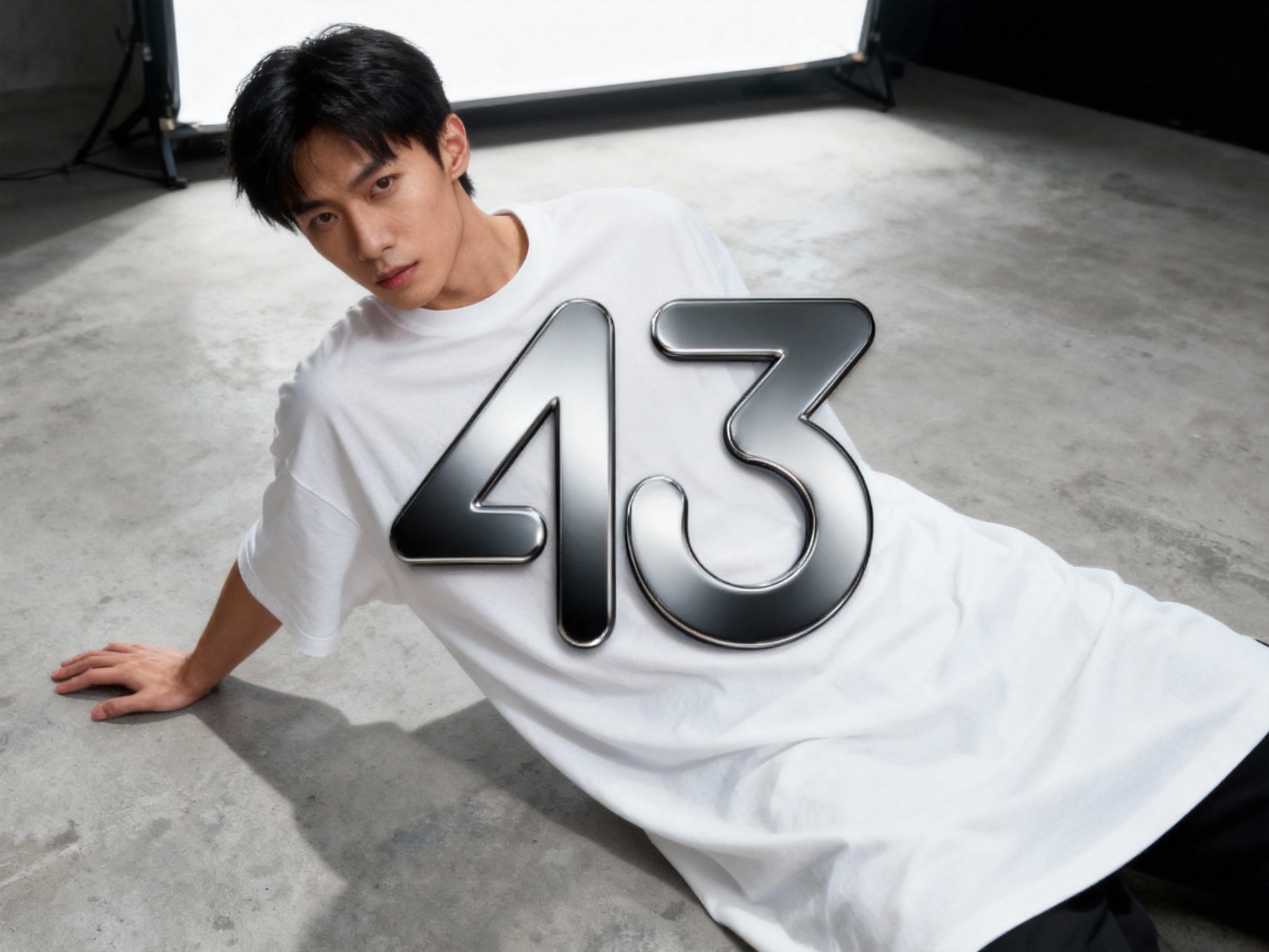 提取参考图的LOGO单独呈现，改为黑色，25岁亚洲男性模特，穿纯白oversizeT恤，黑色LOGO采用烫银工艺（呈现哑光金属质感），俯拍视角，模特单手撑地，T恤自然垂坠，LOGO位于画面中心位置，顶部柔光箱打光，消除多余阴影，背景为极简水泥灰，工业风与高级感融合