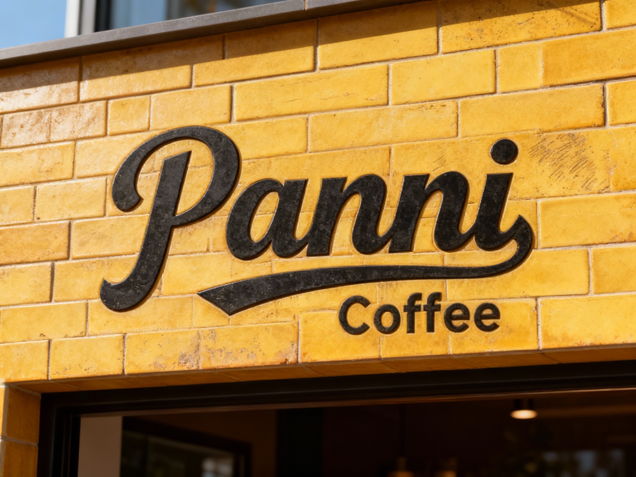 极简黄砖纹门头特写，墙面采用仿黄砖纹理的哑光瓷砖无缝铺贴，底板无做旧粗糙痕迹，LOGO以黑色激光雕刻工艺呈现于砖纹中央，表面做防指纹处理，白天自然光下砖纹质感与LOGO形成对比，适配潮流咖啡门店