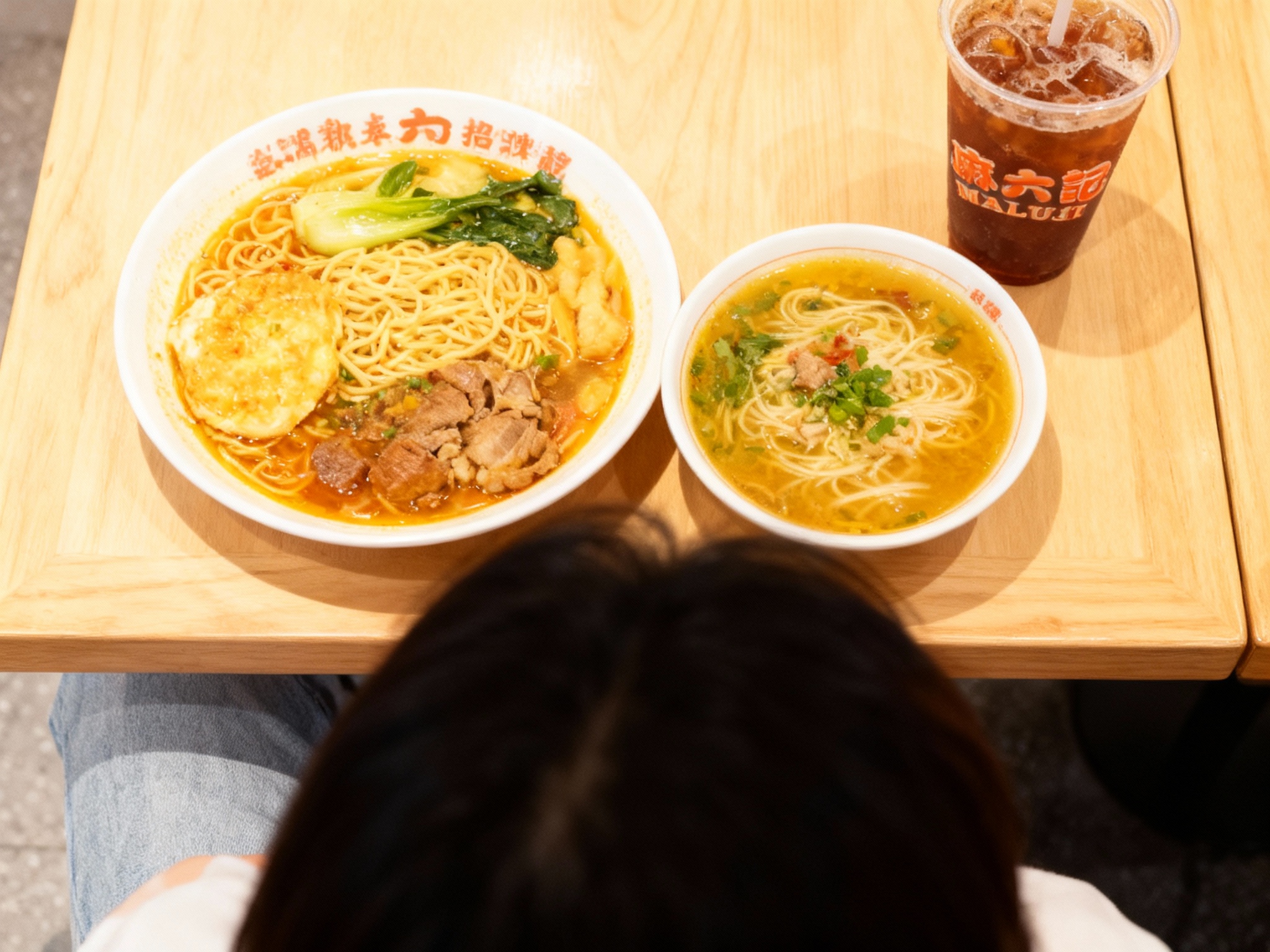 设计社交分享场景图（POV视角）。第一人称视角低头看，面前是一碗摆盘精美的招牌面，汤色诱人。旁边放着一杯冰饮，杯身上印有（智能提取参考图中的LOGO主体并去除原背景）。桌子是浅色实木材质，光影柔和。画面色彩鲜亮，饱和度适中，充满生活气息，极其适合发小红书或Instagram。