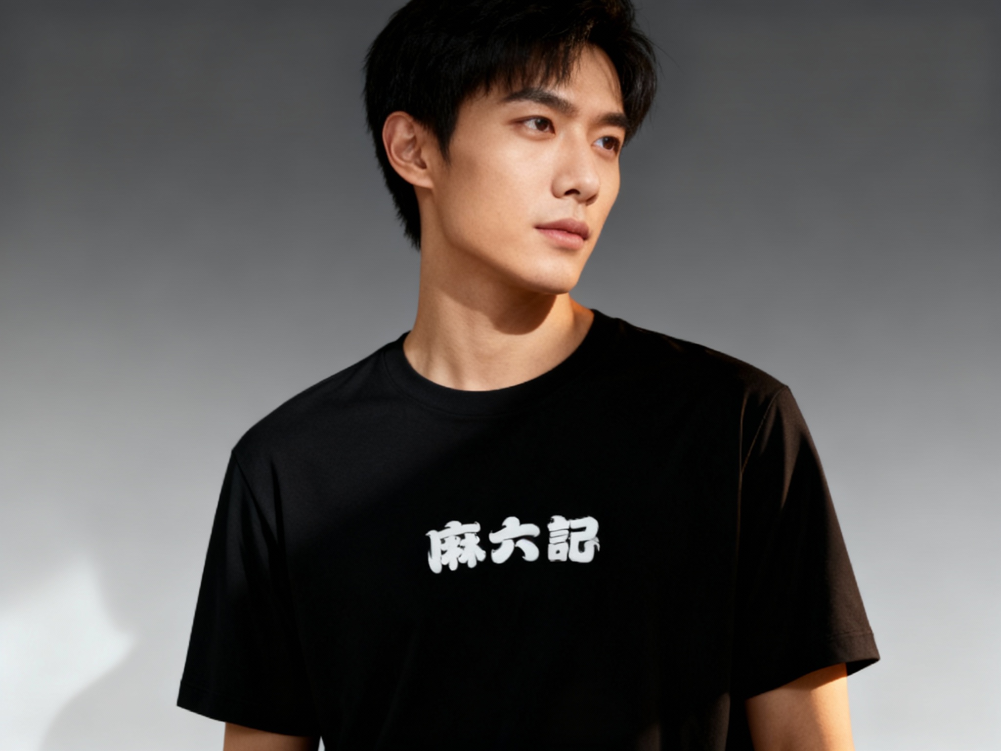 提取参考图的LOGO单独呈现，改为白色，25岁亚洲男性模特，身着纯黑哑光T恤，白色LOGO以胶浆印花工艺呈现在胸口中央，边缘平整细腻，侧逆光拍摄，光线勾勒模特肩部线条，T恤质感柔软垂顺，背景为极简灰色渐变，4A广告大片质感，视觉焦点集中于LOGO