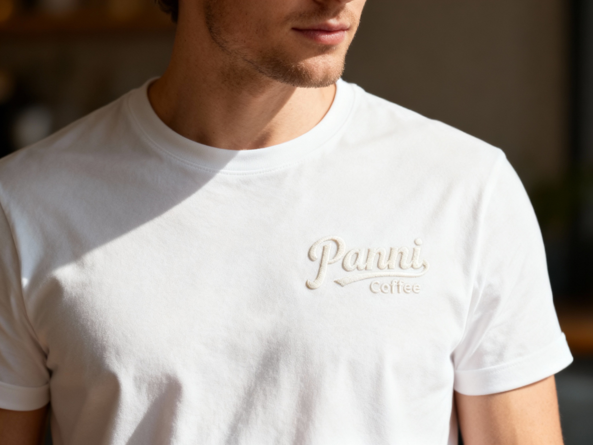 提取参考图的LOGO单独呈现，改为奶白色，25岁欧洲男性模特，身着纯白极简T恤，奶白色LOGO以激光蚀刻工艺呈现，无明显凸起，质感细腻，近距离特写拍摄，聚焦胸口LOGO区域，光线从斜上方射入，凸显LOGO边缘的精致感与T恤的细腻面料，背景虚化，突出产品细节