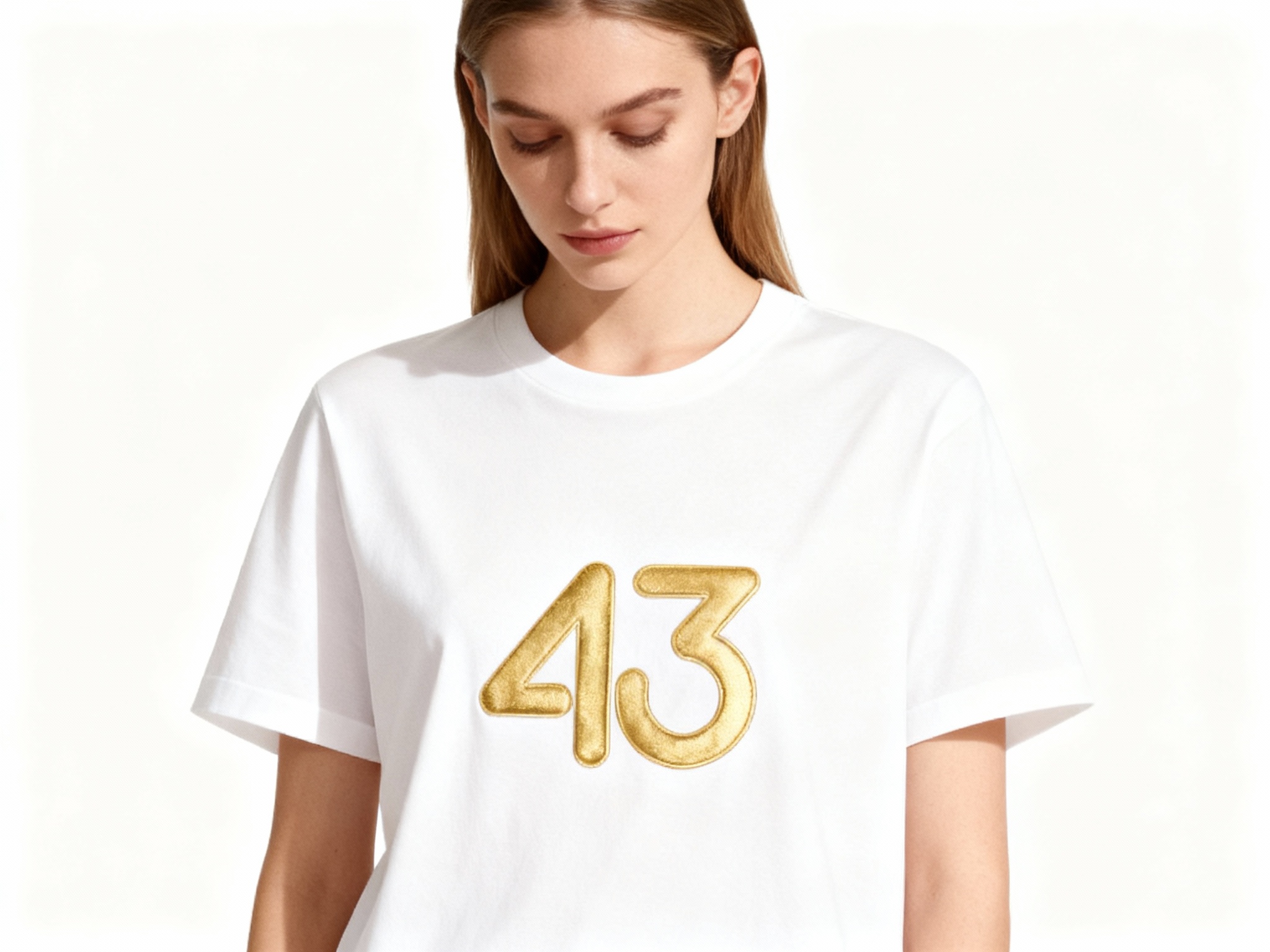 提取参考图的LOGO单独呈现，改为金色，25岁欧洲女性模特，穿纯白重磅T恤，金色LOGO采用烫金工艺印制，金属光泽细腻不浮夸，正面柔光拍摄，光线均匀照亮T恤表面，凸显LOGO与面料的质感对比，模特自然垂眸，背景为纯净白色，画面简洁高级，符合奢侈品广告调性